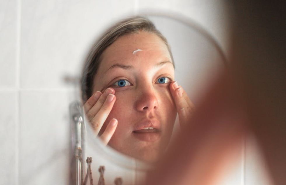 Young woman applying moisturizer in mirror. 