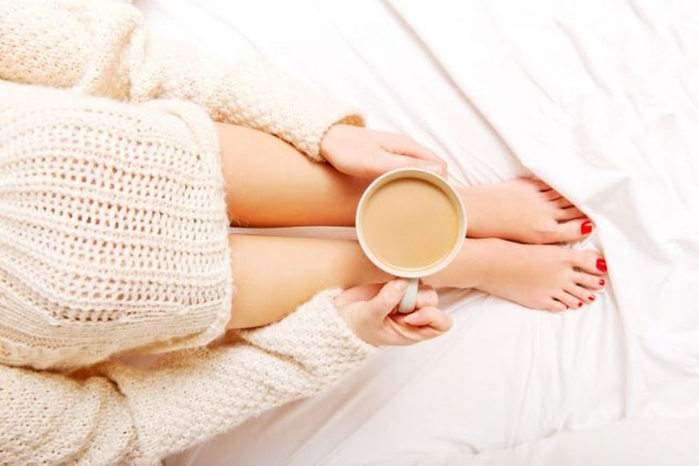 Young woman sitting in bed with a cup of coffee.
