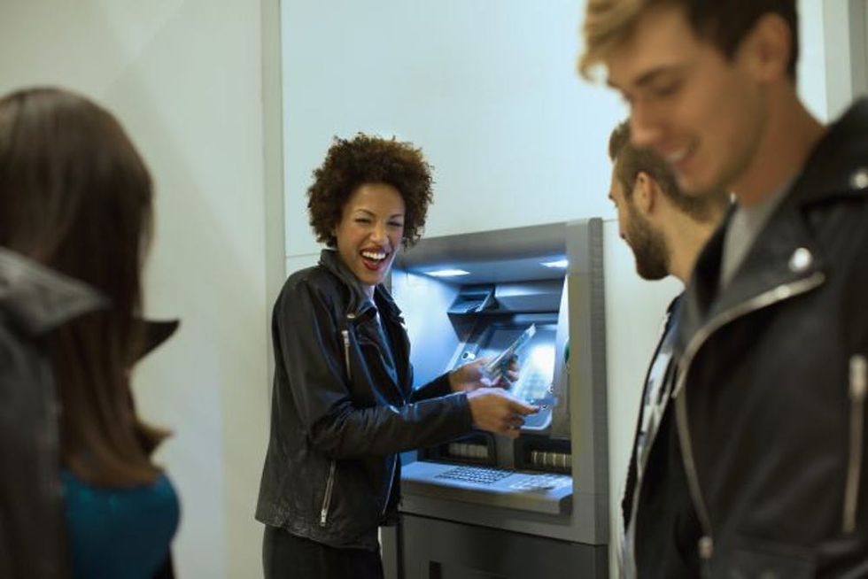 Young woman taking money from cash machine during night out with friends