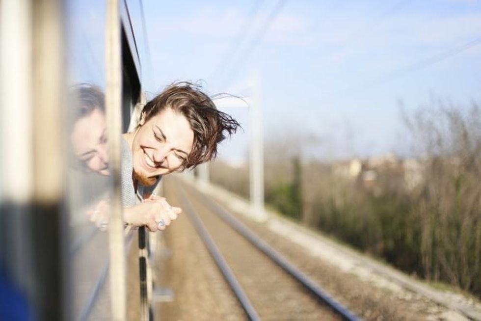 Young woman travelling on a sunny day with her head out the window and the wind blowing her hair