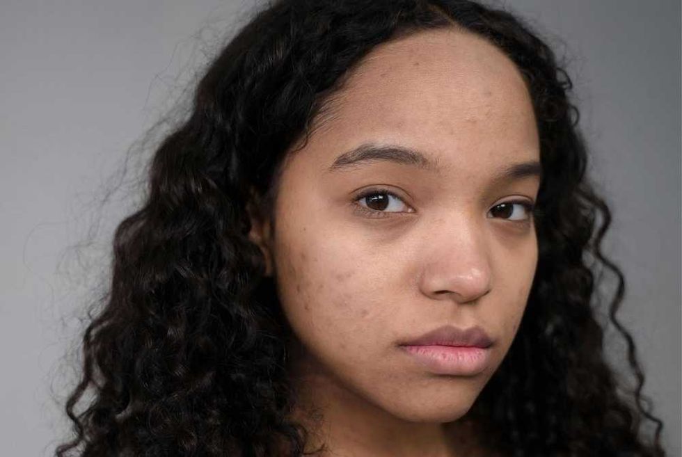 Young woman with curly hair and a serious expression against a gray background.