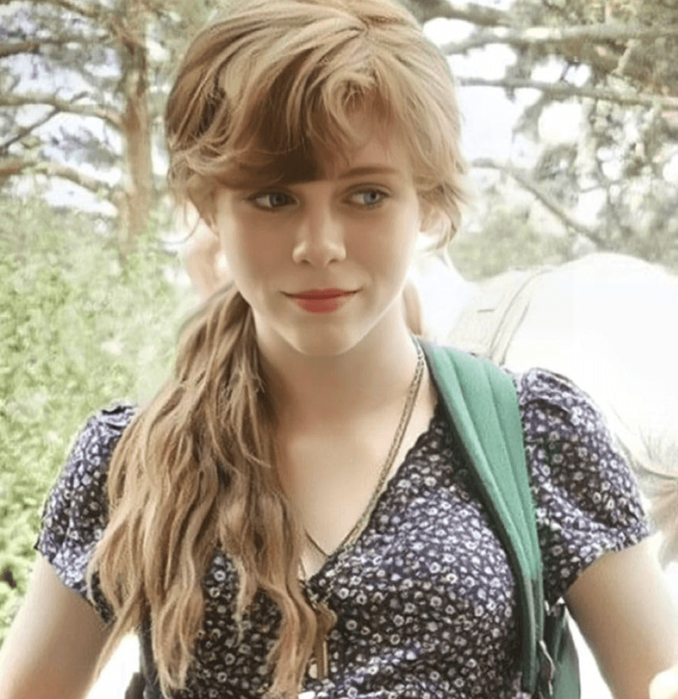 Young woman with long hair, in a floral dress, smiling outdoors.