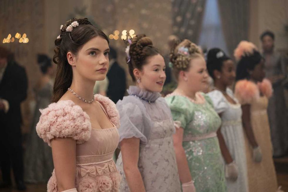 Young women in elegant, pastel Regency dresses at a formal event.